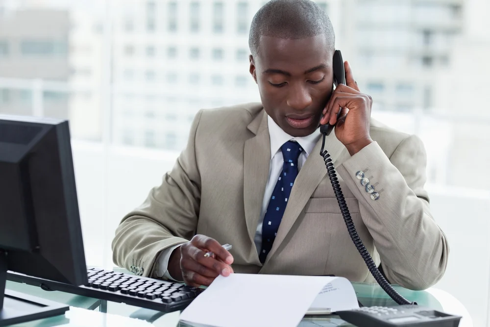Entrepreneur making a phone call while reading a document in his office Entrepreneur making a phone call while reading a document in his office