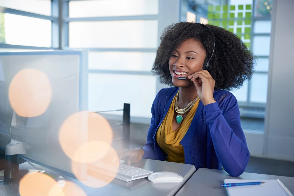 Portrait of a smiling customer service representative with an afro at the computer using headset