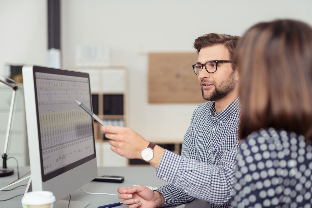 Proficient young male employee with eyeglasses and checkered shirt explaining a business