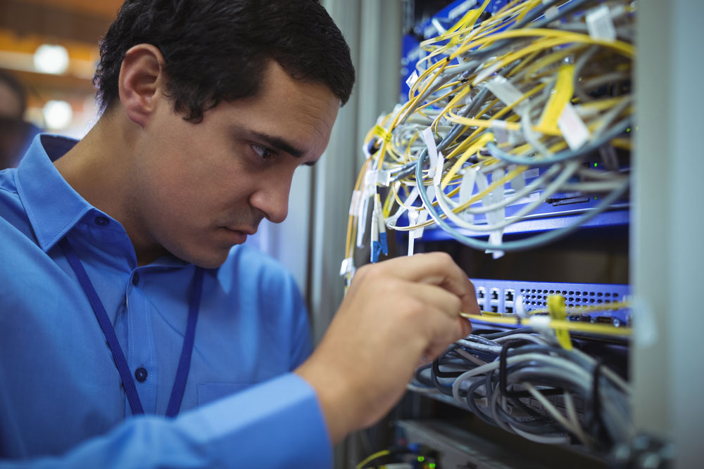 Technician checking cables in a rack mounted server in server room