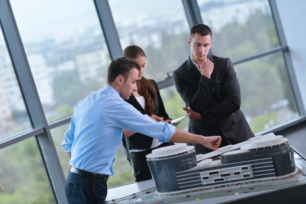 business people group on meeting and presentation in bright modern office with construction engineer architect and worker looking building model and blueprint plans business people group on meeting and presentation in bright modern office with construction engineer architect and worker looking building model and blueprint plans